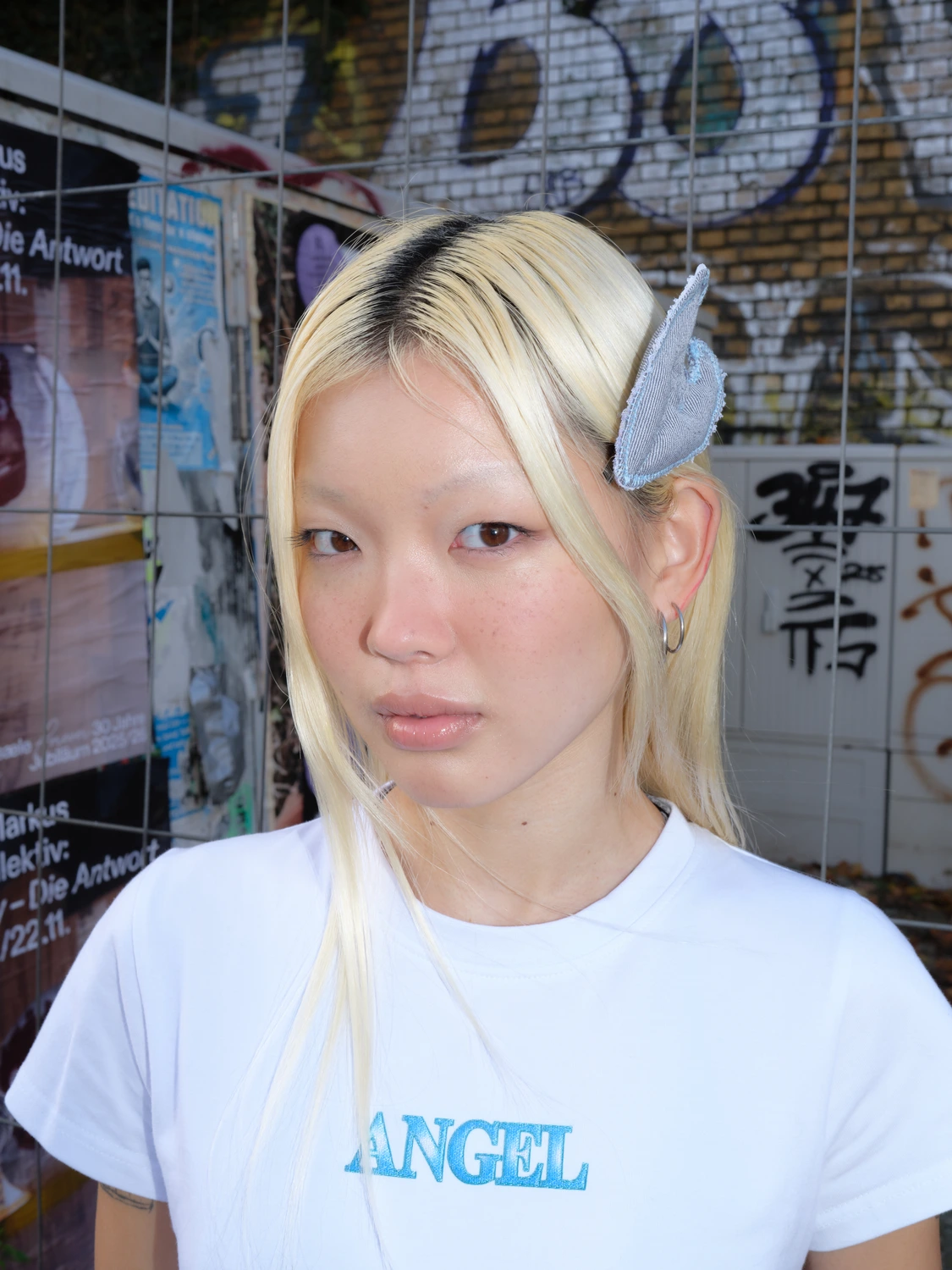 Close-up portrait of model with wing-shaped hair clip against graffiti wall