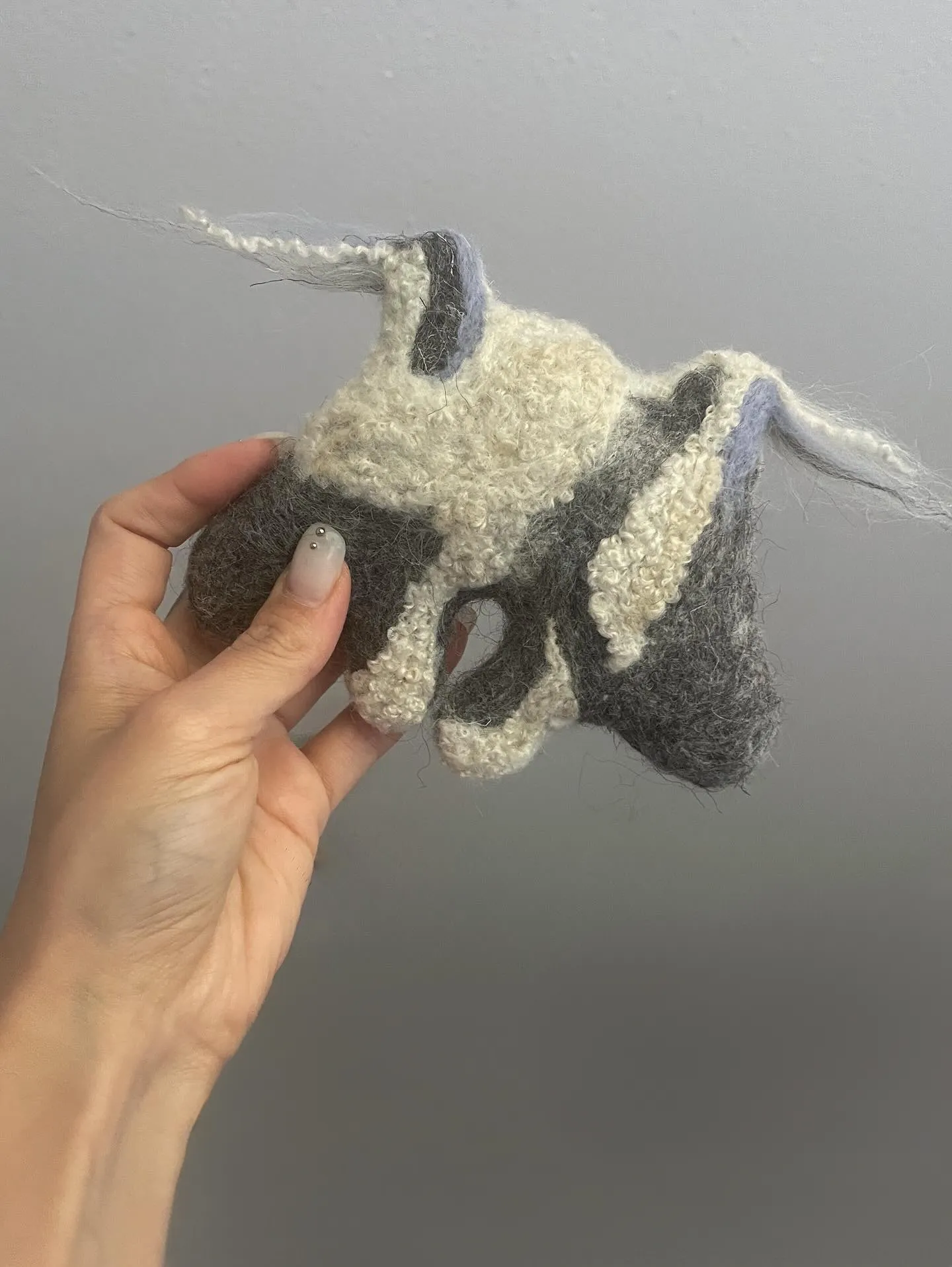 Small protective creature brooch in soft grey tones with gentle face and flowing form